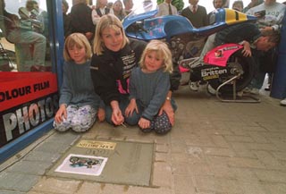 Isabella,Kirsteen (holding nail/pen?), Jessica, bike in background.  For some reason a man is leaning over the rear tire inspecting it?